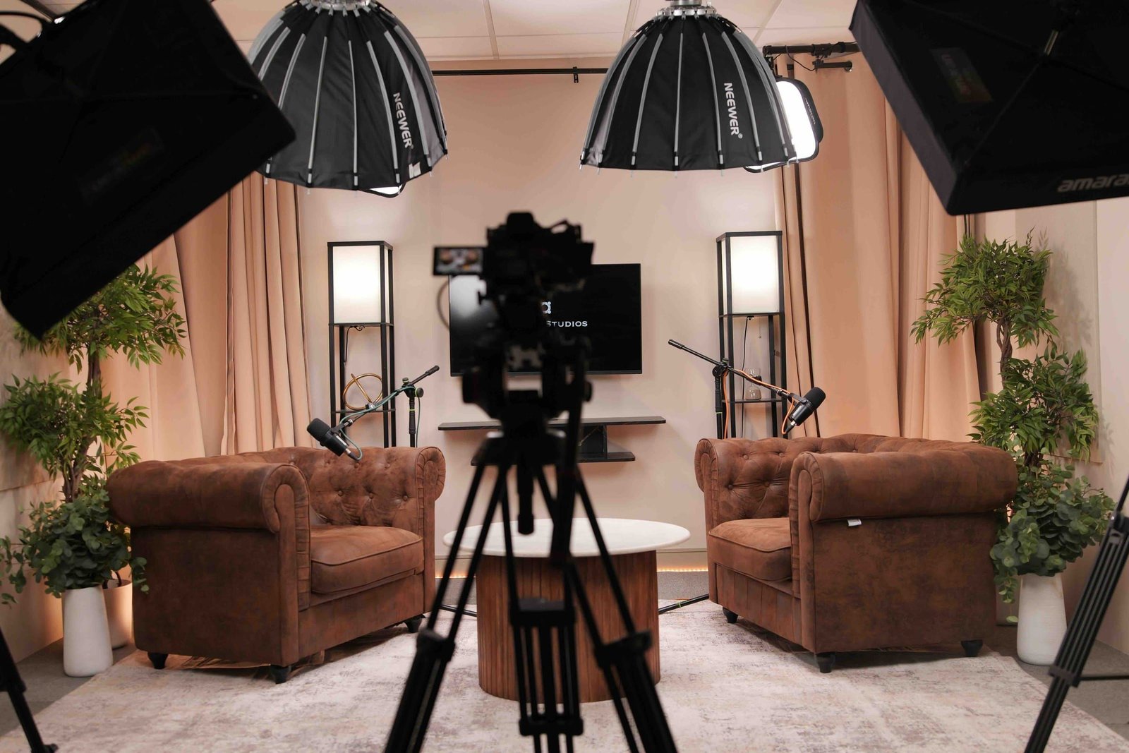 Behind the scenes at Myriad Studios: a camera on its tripod in front of the Room 1 Chesterfields set, with softbox lights overhead